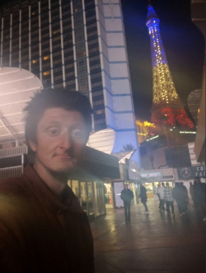 Daniel takes a selfie in front of the replica Eiffel Tower at night.