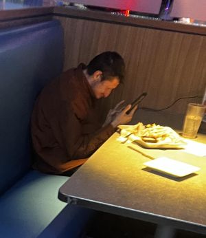 Daniel sitting with very poor posture, hunched and using his phone in front of a plate of fries.